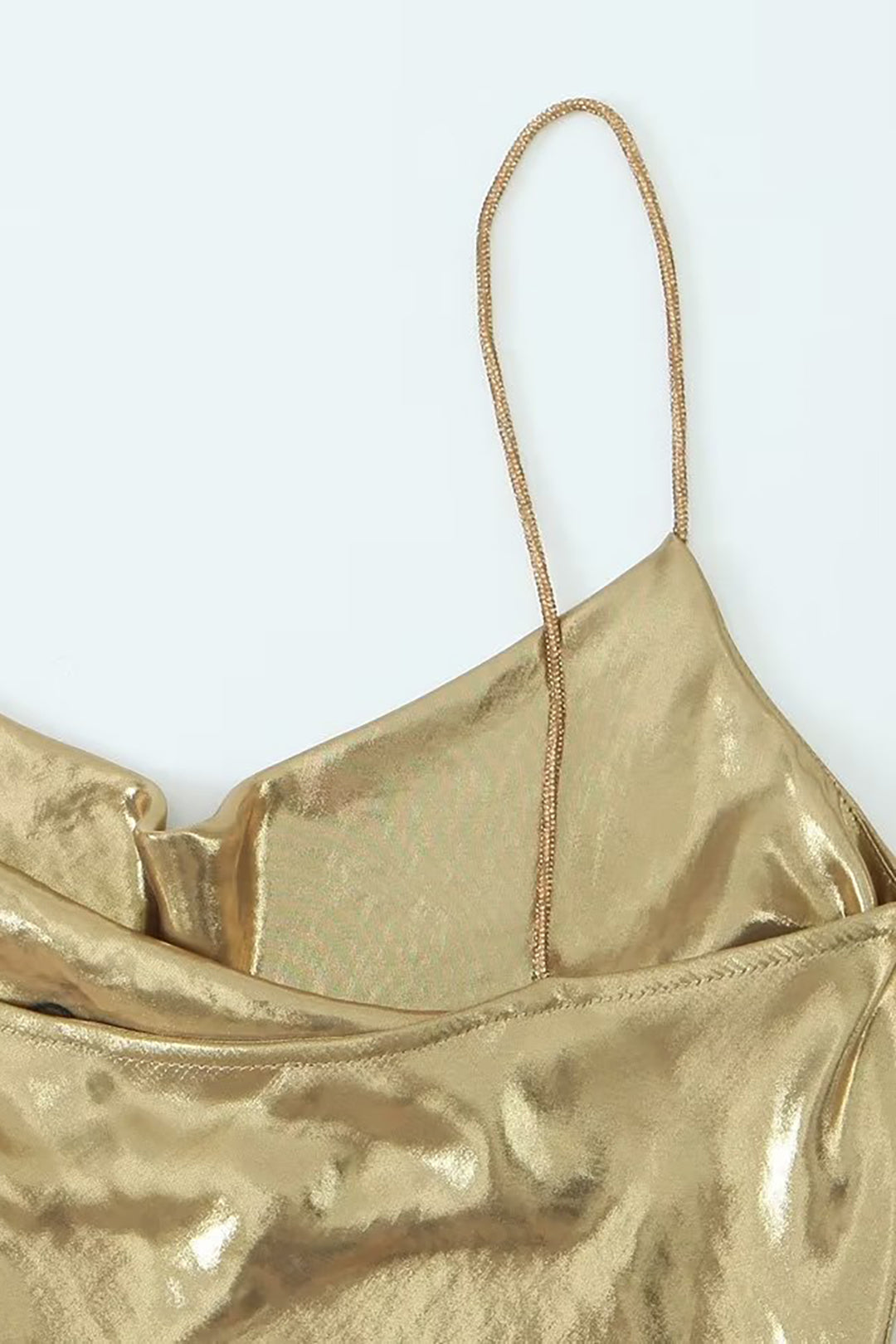 Close-up of the spaghetti strap and cowl neckline of a gold slip dress.