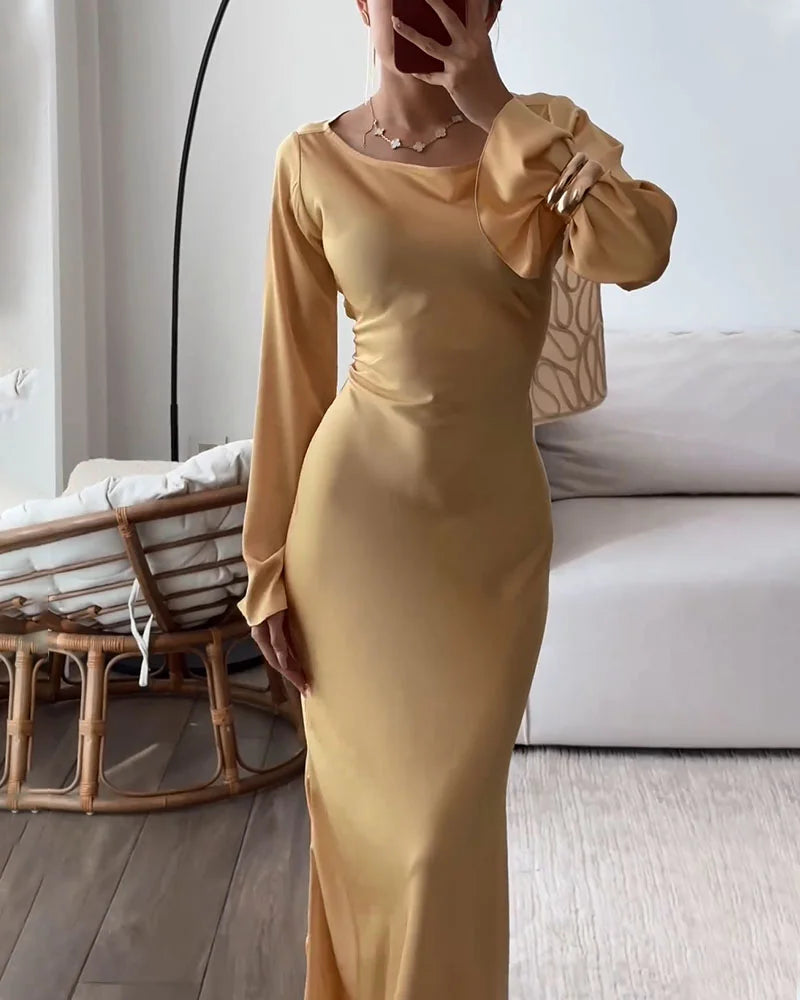 Woman in a gold satin dress with long bell sleeves, holding her arm up to her face.