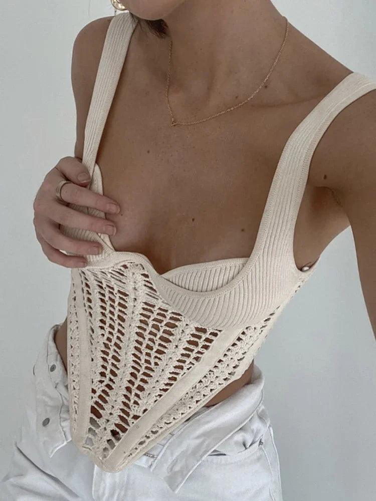 A woman adjusting her cream knit top with a crochet overlay.