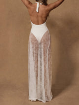 Back view of a woman wearing a white one-piece swimsuit and a sheer white lace maxi skirt.