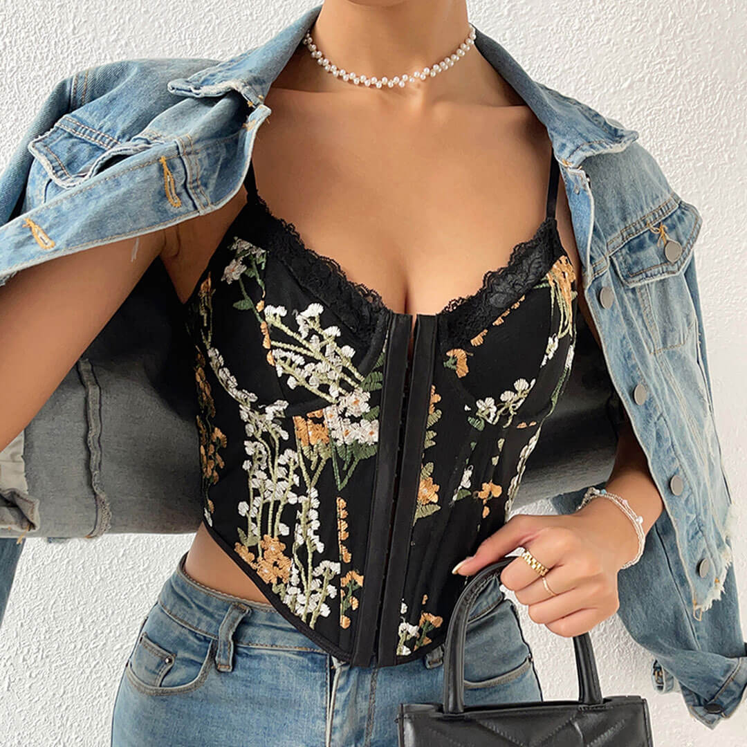 Woman wearing a black floral embroidered corset top with a denim jacket and jeans.