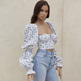 Close-up of a woman wearing a white and blue floral print cropped top with puff sleeves and light blue high-waisted jeans.
