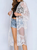 A woman wearing a white lace kimono over a black crop top and denim shorts.