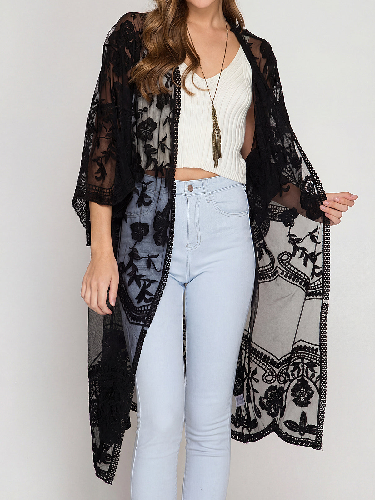 A woman wearing a black lace kimono over a white crop top and light blue jeans.