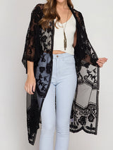 A woman wearing a black lace kimono over a white crop top and light blue jeans.