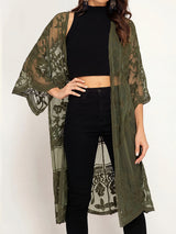 A woman wearing an olive green lace kimono over a black crop top and black jeans.