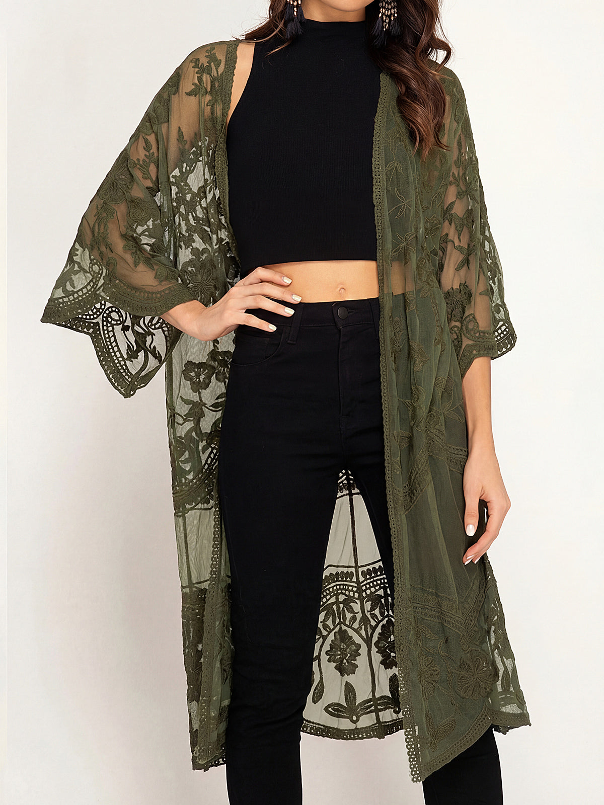 A woman wearing an olive green lace kimono over a black crop top and black jeans.