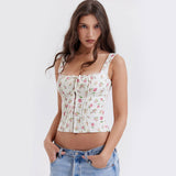 Woman wearing a white floral print corset top with spaghetti straps and a tie front, paired with light wash jeans.