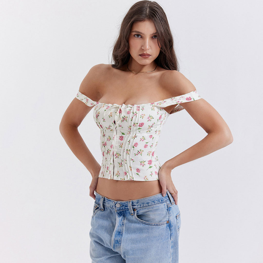 Woman wearing a white floral print corset top styled off-the-shoulder with spaghetti straps, paired with light wash jeans.