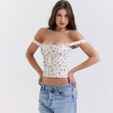 Woman wearing a white floral print corset top styled off-the-shoulder with spaghetti straps, paired with light wash jeans.
