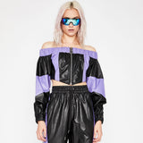 Woman wearing a black and purple off-the-shoulder cropped jacket with a zipper and matching black pants.