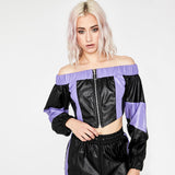 Close-up of a woman wearing a black and purple off-the-shoulder cropped jacket, touching the hem.
