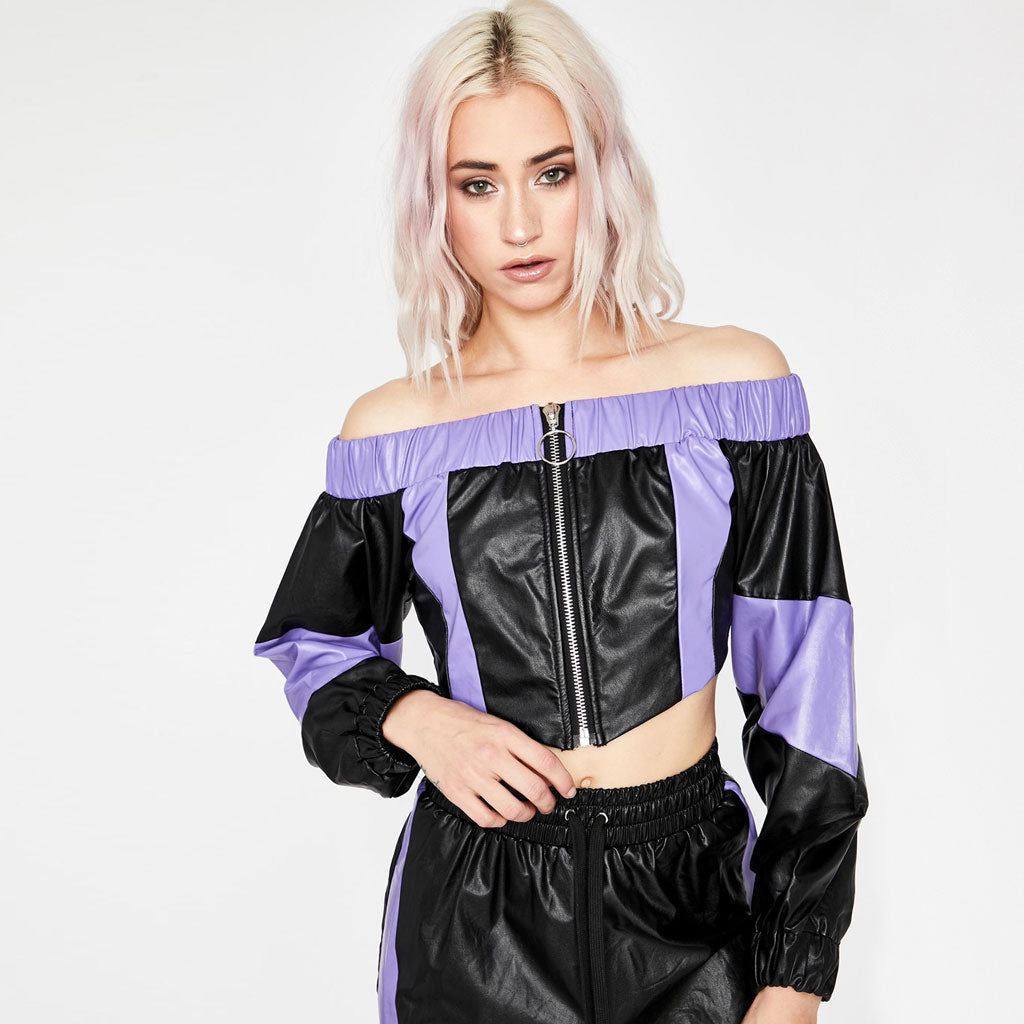 Close-up of a woman wearing a black and purple off-the-shoulder cropped jacket, touching the hem.
