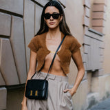 Woman wearing a brown fuzzy cropped cardigan with a gold clasp, black sunglasses, and tan pants.