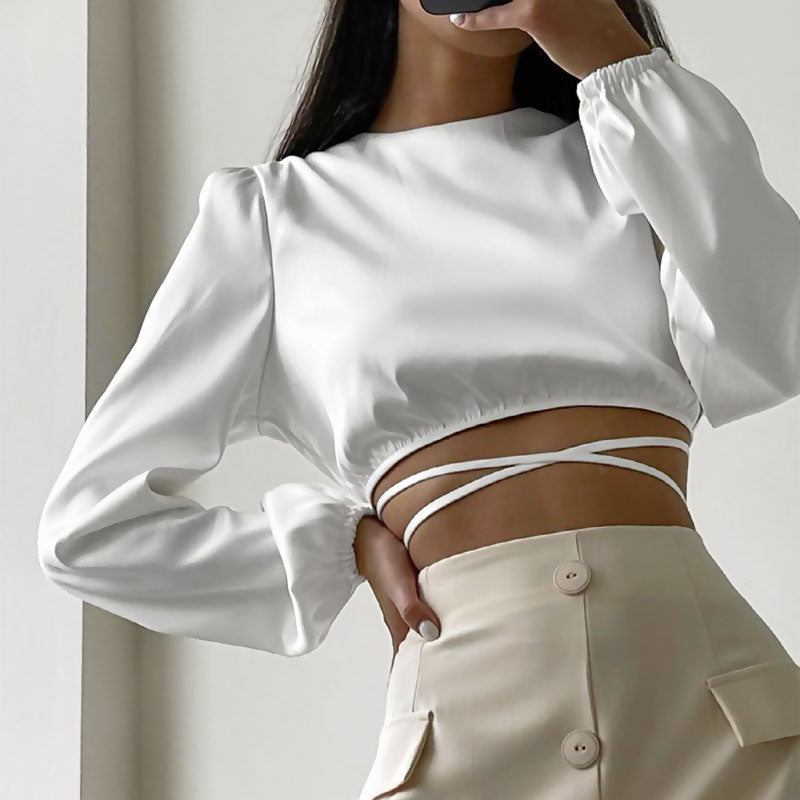 woman wearing a white cropped top with long sleeves tied at the waist with a beige skirt
