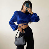 woman in blue crop top and black pants holding a purse