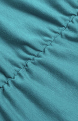 Close-up of the ruched detailing on the skirt of a teal dress.