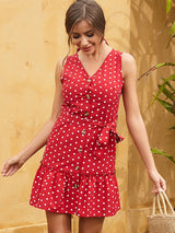 Woman in a red and white polka dot dress, smiling and holding a straw bag.