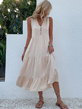 woman wearing a beige tiered midi dress with a v-neck and button details, paired with gladiator sandals