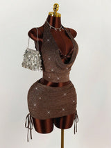 A brown sparkly halter neck crop top and ruched mini skirt set with a drawstring detail on the skirt, shown with a silver fringe purse and dollar sign necklace.