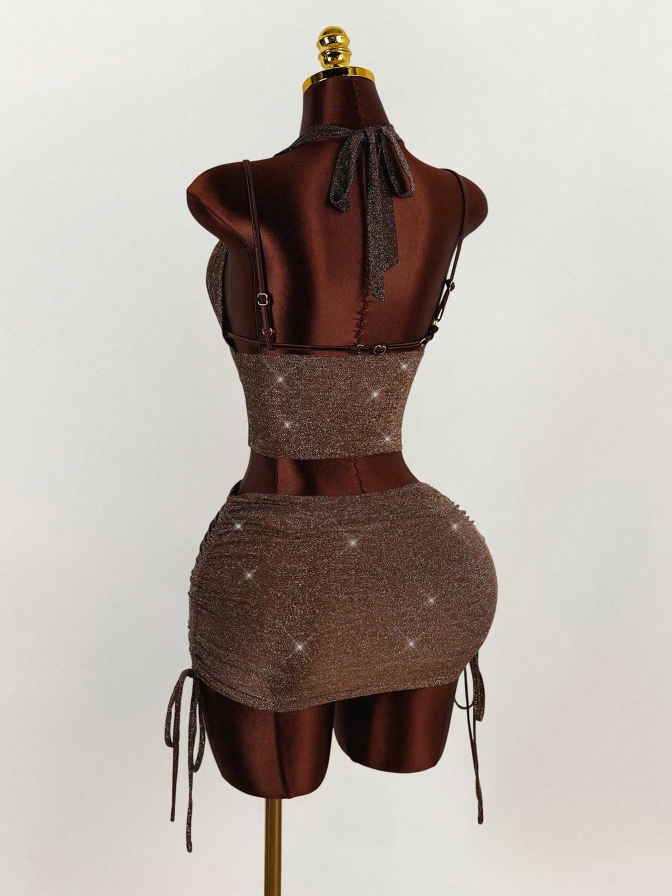 Back view of a brown sparkly halter neck crop top and ruched mini skirt set on a mannequin.