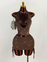 A brown sparkly halter neck crop top and ruched mini skirt set on a mannequin, accessorized with a silver fringe purse and a dollar sign necklace.