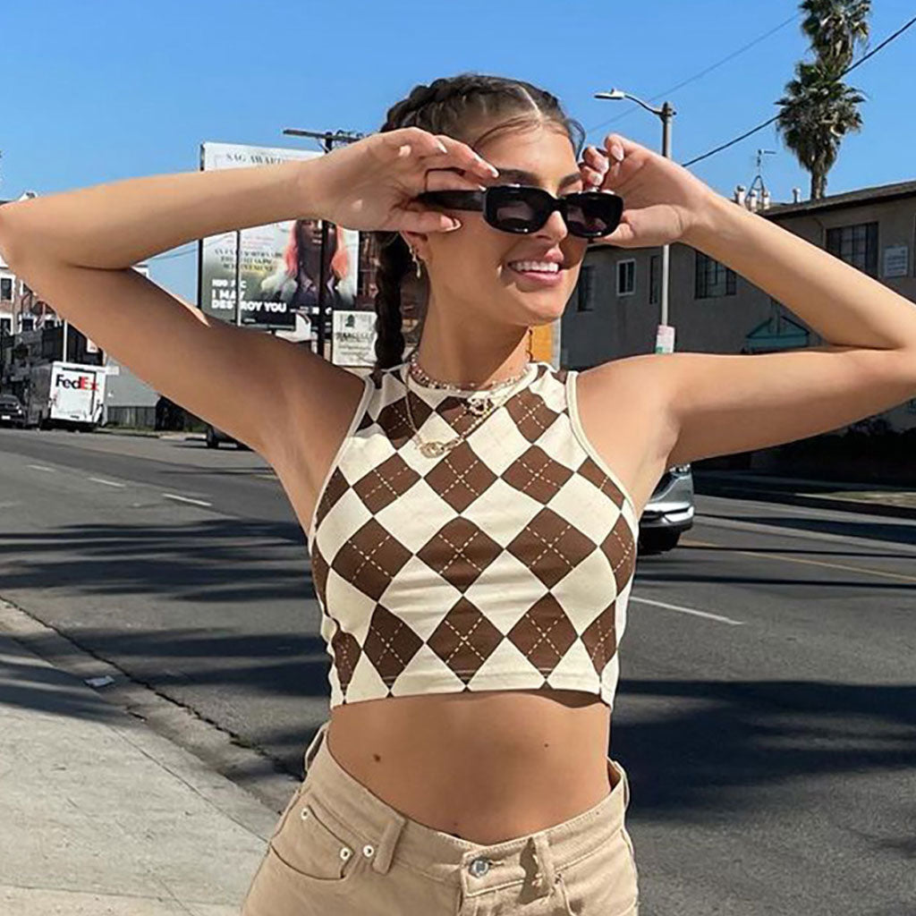 woman wearing a brown and white argyle cropped tank top and tan pants, holding sunglasses