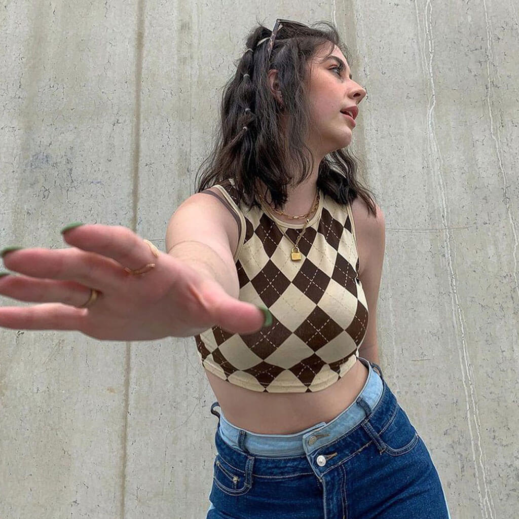 woman wearing a brown and white argyle cropped tank top and blue jeans, reaching out her hand