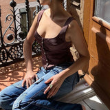 woman wearing a brown satin top and blue jeans sitting on a balcony