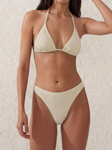Woman wearing a beige textured triangle bikini with a halter neck and high-cut bottoms.