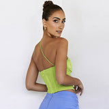 A woman turns her back to the camera, showing the back of a lime green asymmetrical strap top and a blue ruched skirt.