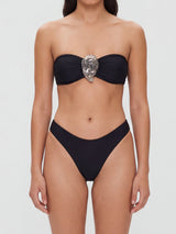 A woman wearing a black strapless bikini with a silver embellishment on the bust.