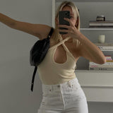 woman in a cream halter top and white jeans holding a black bag