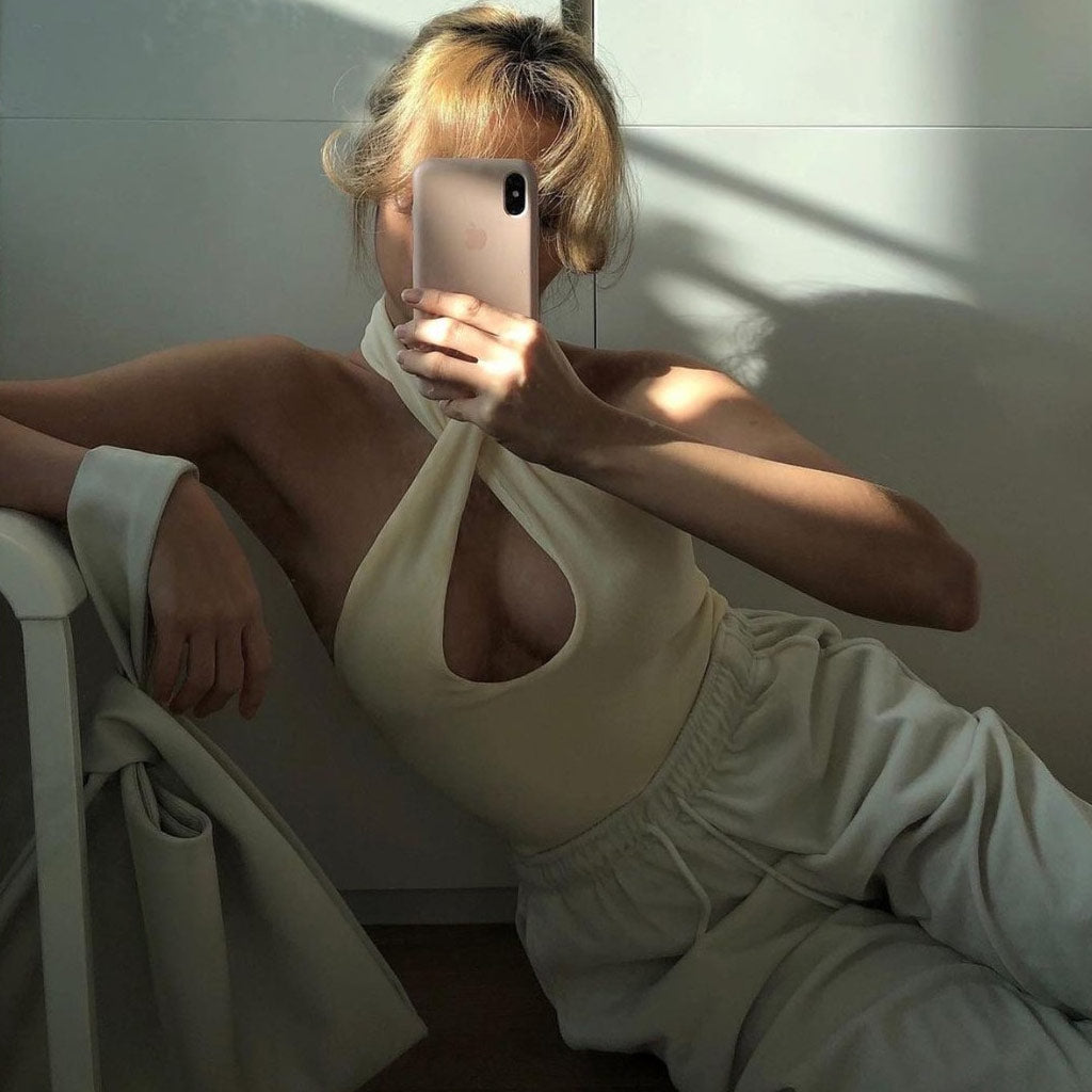 woman in a cream halter top and cream sweatpants holding a pink phone