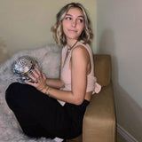 Woman holding a disco ball while wearing a beige knit top and black pants