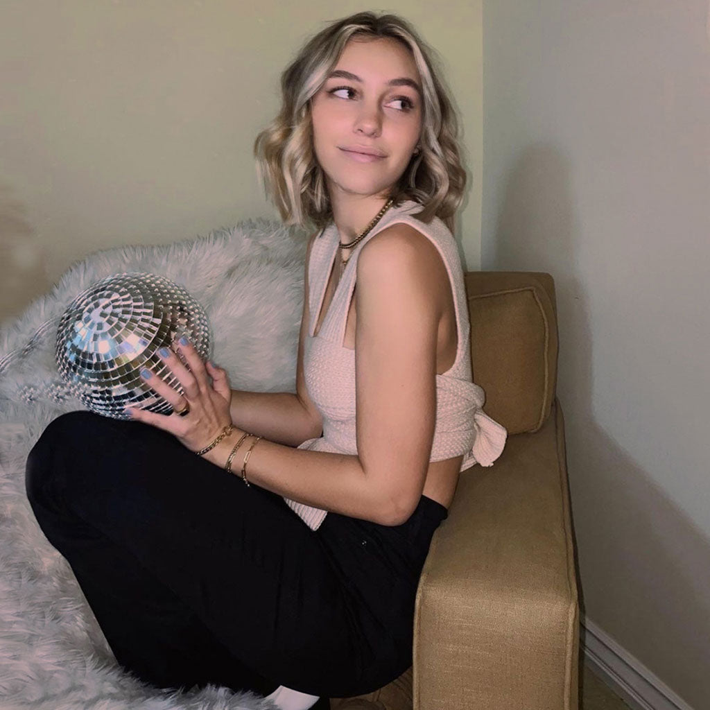Woman holding a disco ball while wearing a beige knit top and black pants