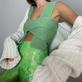 Woman wearing a green knitted wrap top and shiny green pants, with a white cardigan