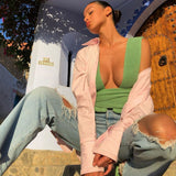 Woman wearing a green knitted wrap top and ripped jeans, with a pink shirt draped over her shoulders, sitting on steps