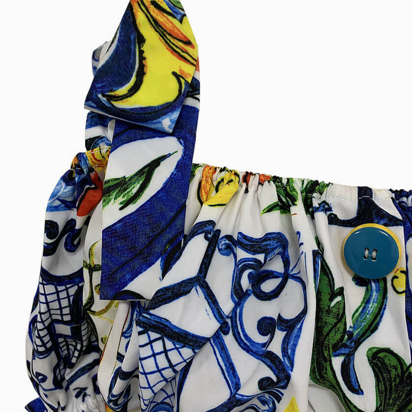 Close-up of the tie shoulder strap on the cropped top, showing the colorful print and blue button detail.