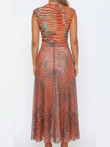 Rear view of a woman wearing an orange and blue patterned sheer maxi dress with a round neckline and sleeveless design.