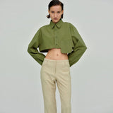 Woman wearing a green cropped button-down shirt with beige pants, hands on hips