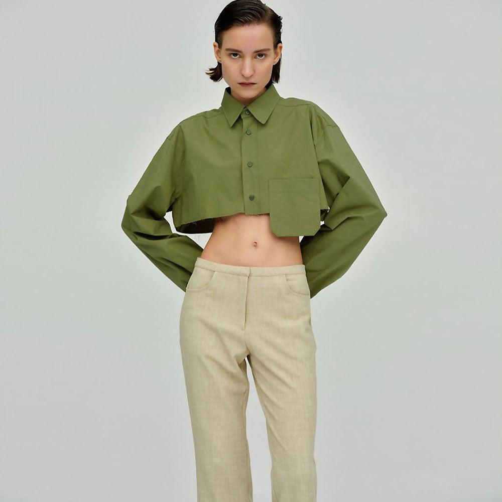 Woman wearing a green cropped button-down shirt with beige pants, hands on hips