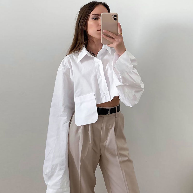 Woman in a white cropped shirt and beige pants taking a mirror selfie