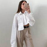 Woman in a white cropped shirt and beige pants taking a mirror selfie
