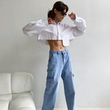Woman in a white cropped shirt and light blue cargo pants posing with sunglasses