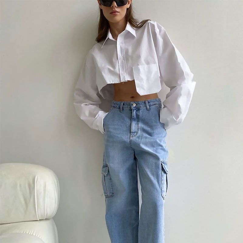 Woman in a white cropped shirt and light blue cargo pants standing against a wall