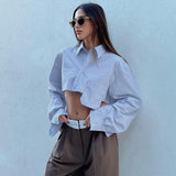A woman in a white cropped button-down shirt and brown wide-leg pants, wearing sunglasses.