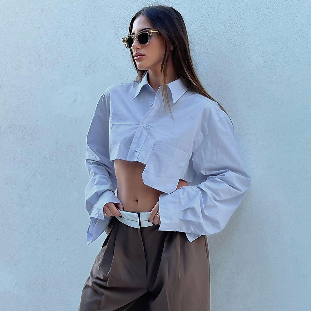 A woman in a white cropped button-down shirt and brown wide-leg pants, wearing sunglasses.
