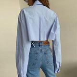 Back view of a woman in a light blue cropped button-down shirt and jeans.