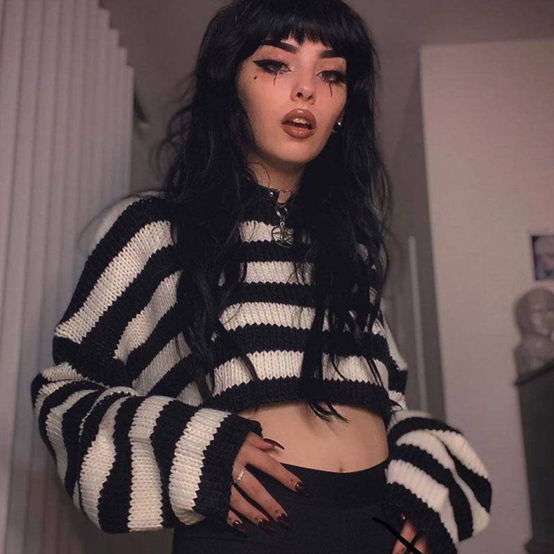 A person with dark hair and dramatic eye makeup wearing a black and white striped cropped sweater.